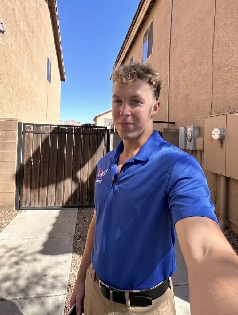 Hayden Mitchell during his in-home sales years, photographed on a residential estimate. Wearing a blue company polo and khakis between two stucco homes, electrical meters and a wrought-iron gate behind him, bright Arizona daylight.
